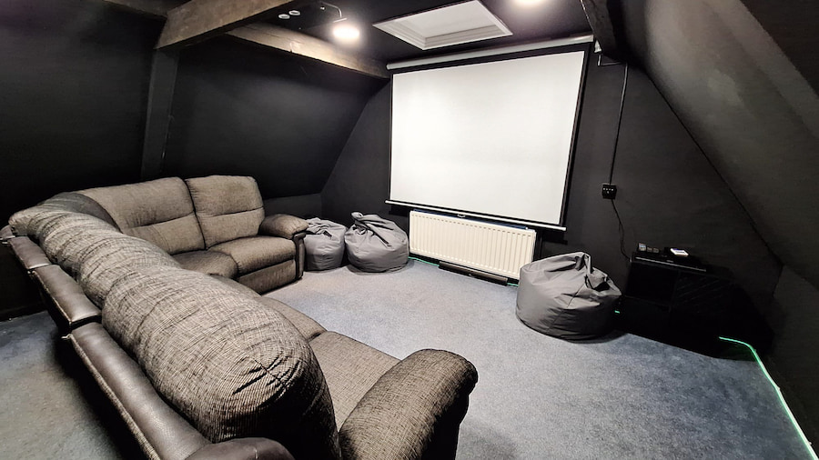 A cinema room painted black with a screen and large corner sofa with bean bags.
