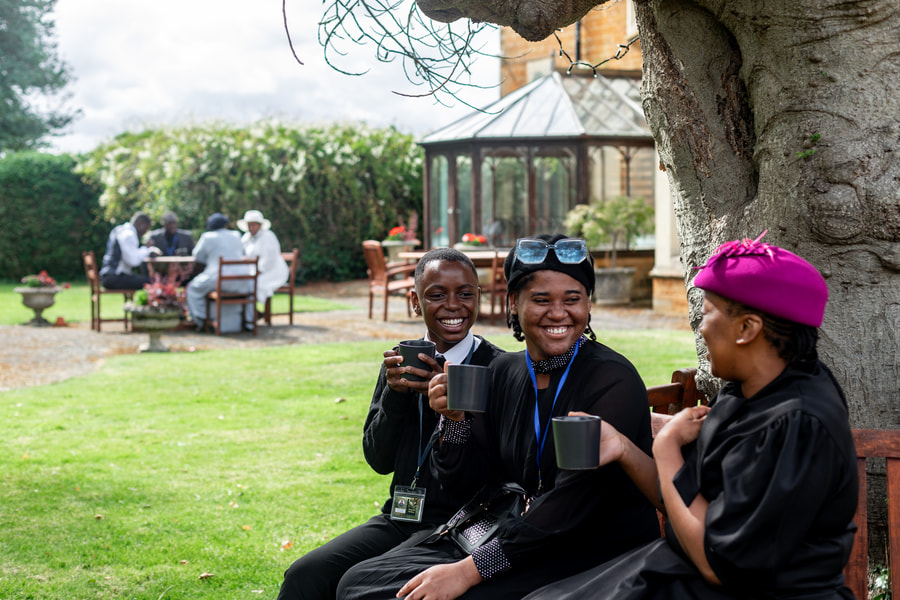 3 delegates sitting outside one of our venues with a cup of coffee, laughing together.