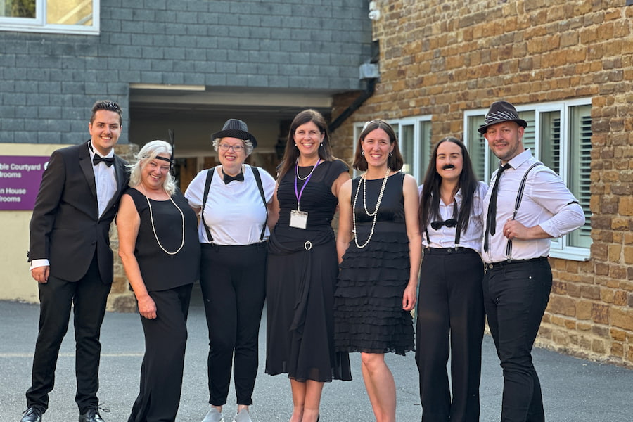 A group of the attendees lined up in their 1920s wear smiling at the camera.