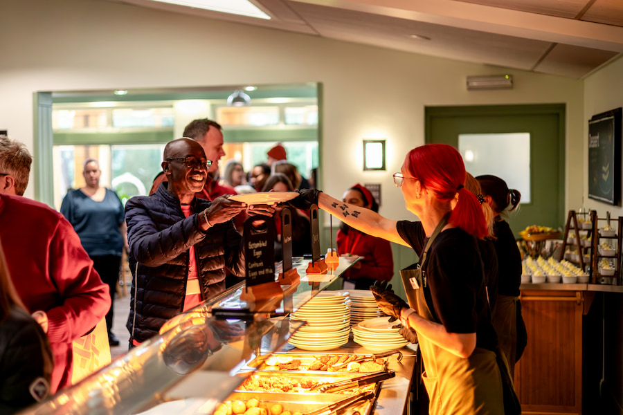 A member of the dining staff handing a plate of food to a smiling Christian Aid guest.