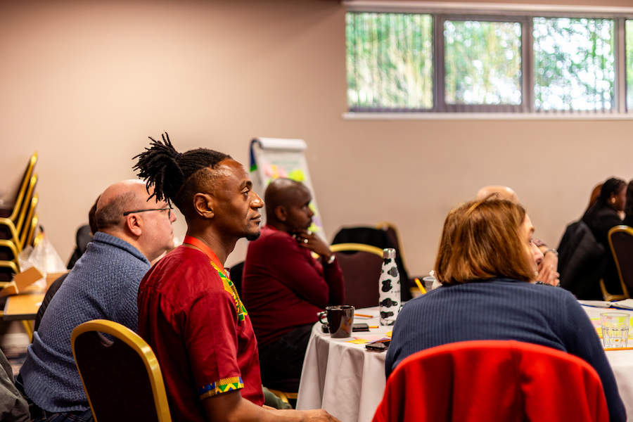 A man sitting on a table with other Christian Aid workers during a session, looking to the front.