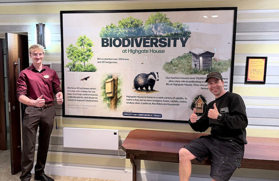 2 of our staff standing next to our biodiversity poster which is located in the dining room.