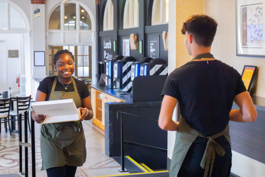 2 members of staff smiling at each other as they pass one another in the hallway.