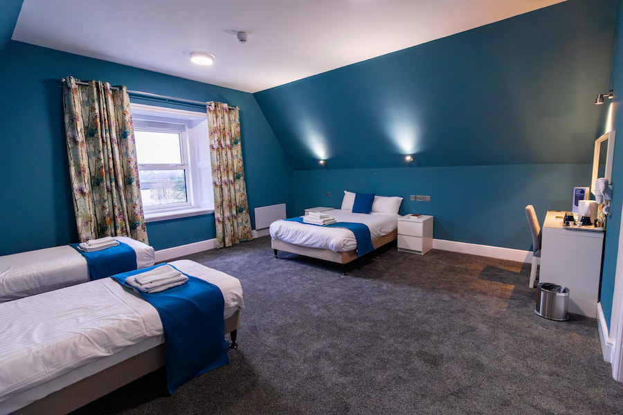 The family bedroom showing a double bed and 2 single beds with bright blue walls and cosy lighting.