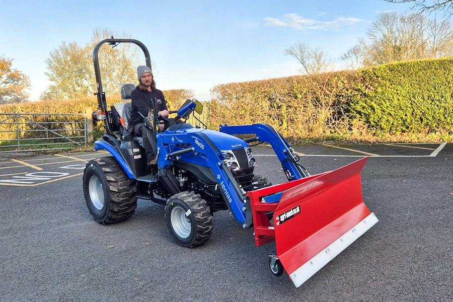 A blue tractor with a red snow plow with one of The Hayes' maintenance team sitting on it.